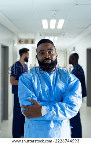 Vertical portrait of smiling biracial male healthcare worker in busy hospital corridor, copy space. Hospital, medical and healthcare services.