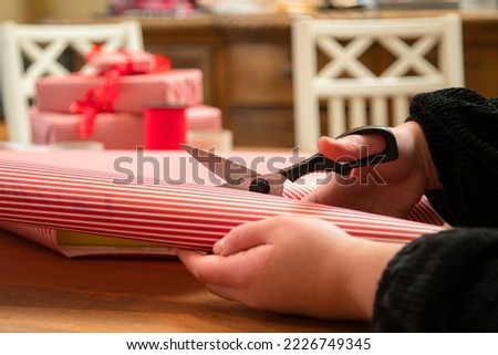 Woman wrapping a gift in stripped paper with red ribbon. Hands packing a box in the red and white christmas paper.