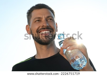 Happy man with bottle of water outdoors on hot summer day. Refreshing drink