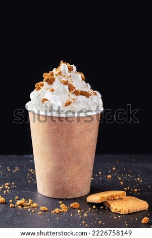Paper cup with hot drink with whipped cream and gingerbread cookie on dark background. Recycling and eco friendly concept.