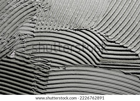 Gray wall glue plaster comb surface prepared for tiling. Tile adhesive notched trowel patterns. Texture background of tile mortar paste. Grey cement wall with a linear pattern. Macro shot. Royalty-Free Stock Photo #2226762891