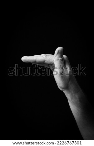 Dramatic black and white  image of a male hand fingerspelling the Arabic sign language letter 'خ' or 'Kha', isolated against a dark background.