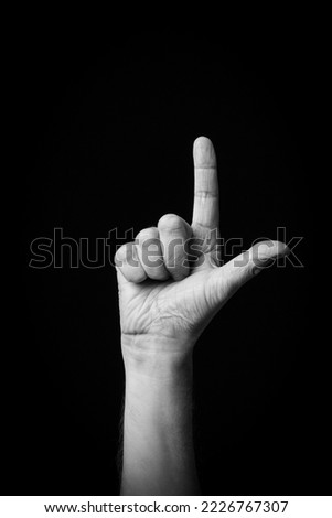 Dramatic black and white  image of a male hand fingerspelling the Arabic sign language letter 'ل' or 'Lam', isolated against a dark background.