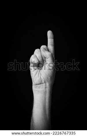 Dramatic black and white  image of a male hand fingerspelling the Arabic sign language letter 'ب' or 'Ba', isolated against a dark background.