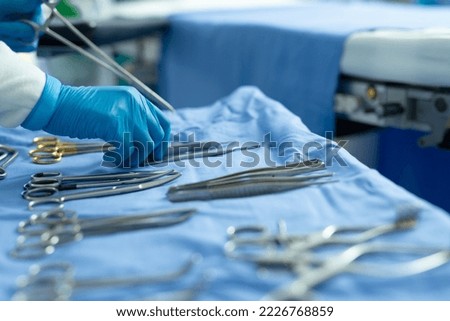 Gloved hand of surgical tech placing tools on table in operating theatre, with copy space. Hospital, medical and healthcare services. Royalty-Free Stock Photo #2226768859