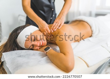 Young modern beautiful Latin girl lying on her stomach and being massaged by unrecognizable professional beautician. Beauty salon interior. Relaxation concept. High quality photo