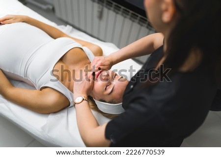 Traditional face-lift massage concept. Relaxation and free time activities. Professional caucasian aesthetician performing face massage on her beautiful female pregnant client. . High quality photo