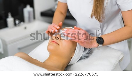 Beautiful unrecognizable Asian woman lying down on SPA bed. Unrecognizable caucasian long-haired beautician doing deep cleansing of false lashes of her female client. High quality photo