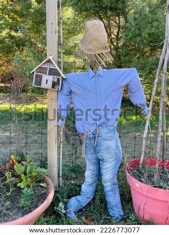 A faceless scarecrow next to a bee box and potted plants.