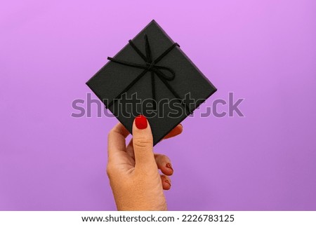 woman's hand with red nails holding black gift over purple wall