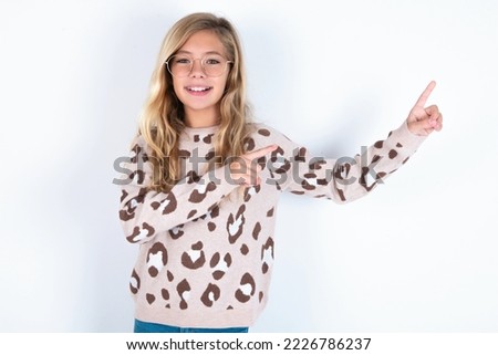 Positive caucasian teen girl wearing animal print sweater over white background with beaming smile pointing with two fingers and looking on empty copy space. Advertisement concept.