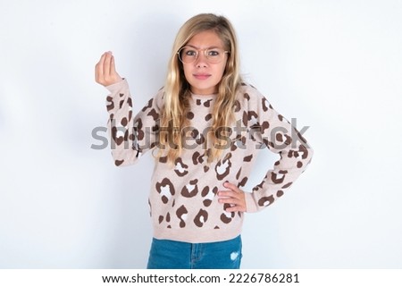 What the hell are you talking about. Shot of frustrated caucasian teen girl wearing animal print sweater over white background gesturing with raised hand doing Italian gesture, frowning, 