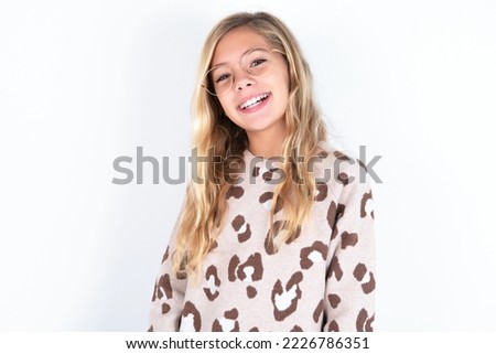 caucasian teen girl wearing animal print sweater over white background with broad smile, shows white teeth, feeling confident rejoices having day off.