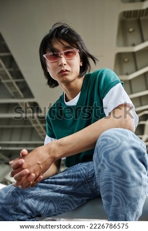 Vertical portrait of street style Asian man looking at camera outdoors and wearing pink sunglasses Royalty-Free Stock Photo #2226786575