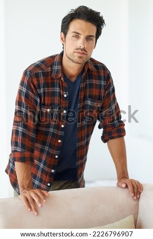 Hes handsome and headstrong. Portrait of a gorgeous young man standing behind a sofa and looking at the camera.