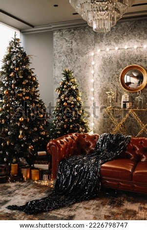 The concept of Christmas. Luxury expensive interior with a leather sofa, a Christmas tree and decorative festive elements on a dark background in the living room of the indoor house. Selective focus