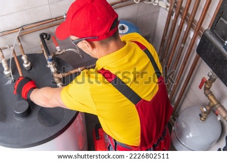 Professional Caucasian Plumber Repairing Tank Water Heater in Boiler Room of Commercial Building. Heating Equipment Maintenance Theme. Royalty-Free Stock Photo #2226802511