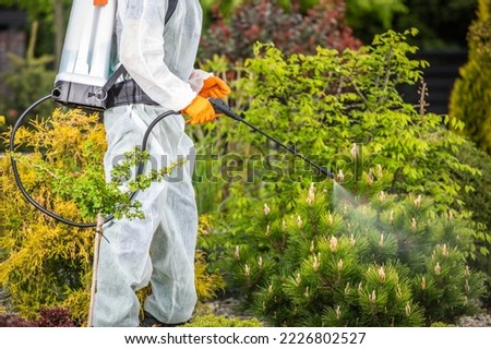 Professional Gardener in Safety Uniform Spraying Pesticides on Plants Using Pump Sprayer. Gardening Theme. Royalty-Free Stock Photo #2226802527