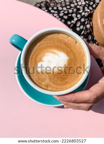 Young woman in silk dress is drinking latte art coffee. Young candid woman drinking morning coffee in tiffany color ceramic mug with saucer on cafe terrace. High quality photo