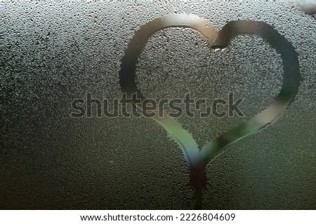 Condensation on the window from a sudden change in temperature outside and inside the house, a heart painted on the glass.