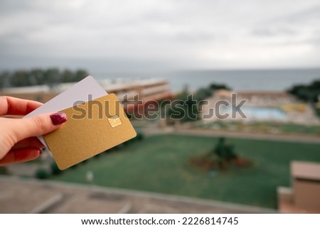 Golden and White Bank Card In Woman Hand On Background Of Hotel Bungalow And Pool In Moraitika, Corfu, Greece. The Concept Of Payment For Relax And Unlimited Possibilities. High quality photo