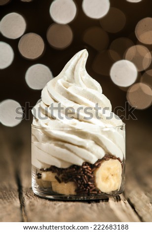 Delicious party dessert of sliced fresh banana and chocolate sprinkles topped with a swirl of low-fat frozen yogurt on a rustic wooden counter with a bokeh of sparkling lights