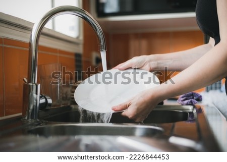 Woman washing dishes in kitchen sink, close up of hands rinsing plate. Royalty-Free Stock Photo #2226844453