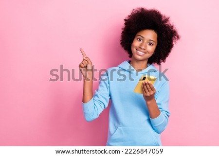 Photo portrait of cute school girl hold gadget point empty promo space dressed stylish blue garment isolated on pink color background