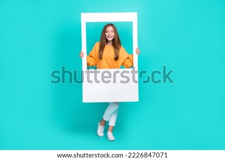 Full length photo of sweet pretty schoolgirl wear orange sweatshirt holding white photo frame isolated turquoise color background