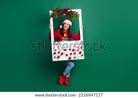 Full length photo of pretty dreamy girl dressed ugly print red x-mas pullover rising decorations window empty space isolated green color background