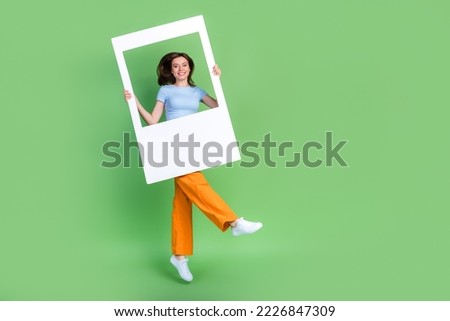 Full size photo of energetic pretty girl jumping arms hold paper album card isolated on green color background