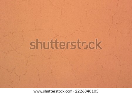 Photo of a peach colored concrete wall with many cracks in the plaster