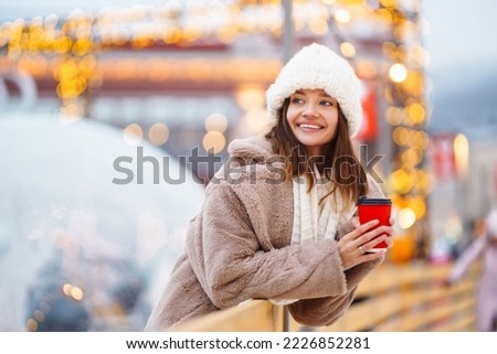 Happy woman with disposable paper coffee cup in winter over outdoor ice skating rink on background. Christmas, hot drinks and holidays concept.
