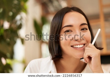 Close up portrait of stylish young brunette woman, sitting with graphic pen and smiling, relaxing in cafe, writing something, making notes.