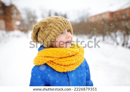 Admire little boy walking on sunny winter day. Emotional child dressed in a warm clothes, hat, hand gloves and scarf. Active outdoors leisure for family with kids on nature among driven snow
