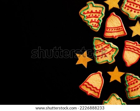 Christmas side border of homemade colorful gingerbread cookies in shape of christmes tree and bell, golden star on black background. Xmas greeting card with copy space. View from above. Flat lay.