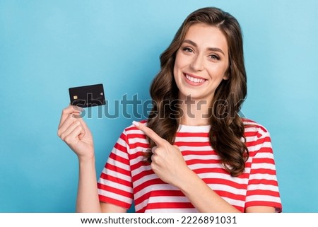 Photo of cute positive girl dressed red t-shirt smiling pointing finger credit card isolated blue color background