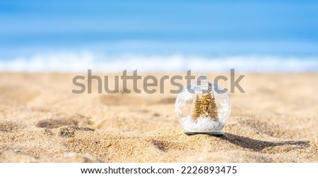 Golden Christmas tree in snow globe with blue blurry background on the beach with shiny day, Christmas banner, Christmas banner, happy concept, copy space, soft focus