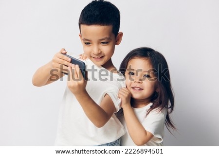brother and sister take a selfie on their fashionable smartphone while standing in white T-shirts on a light background sideways to the camera