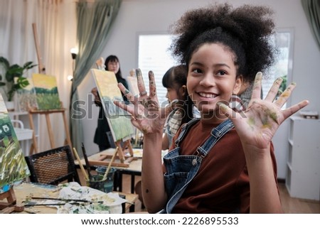African American girl shows hand messed up with acrylic colors, joy, and fun learns with student children in art studio of an elementary classroom, creative painting with skills in school education. 