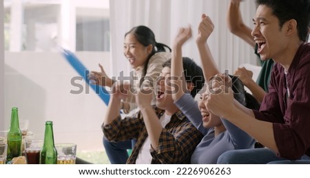 Group of young adult friend man and woman asia people sit at sofa couch joy chanting party fun game FIFA world cup live TV at home eat snack bowl drink beer bottle glass jump mad happy win exult face. Royalty-Free Stock Photo #2226906263