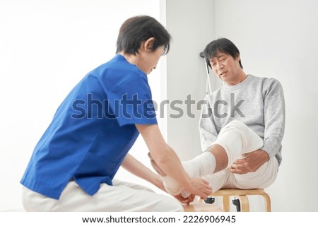Asian nurse bandaging a patient's ankle