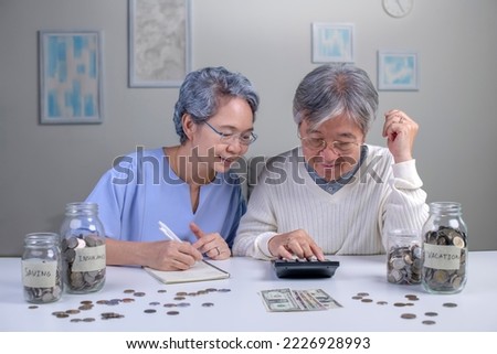 Savings concept. Asian old elderly senior couple grandparents husband and wife saving money, economizing 
pension, putting coin into money box, thinking over pension plan Royalty-Free Stock Photo #2226928993