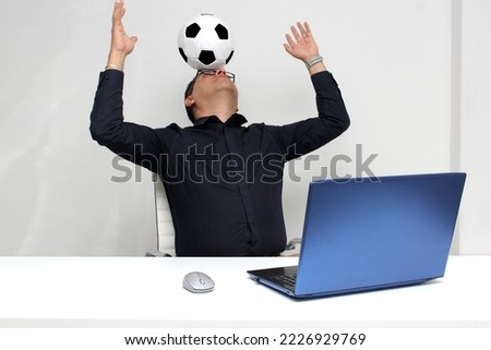 Latino adult office man watches football games on his work laptop during office hours in the morning, he sees him excited, nervous, surprised next to his soccer ball

