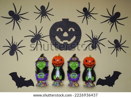 Scary Halloween figurines stand on a light background in close-up, behind hangs terrible pumpkin. Cute character in monster costume. Halloween concept. Holiday decoration toys