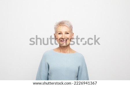 Elderly beautiful woman with a short pixie haircut in a blue sweater on a gray background Royalty-Free Stock Photo #2226941367