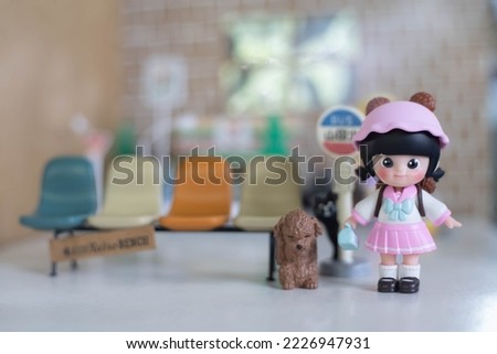 Cute doll in pink dress waiting for bus coming with her dog, selection focus.