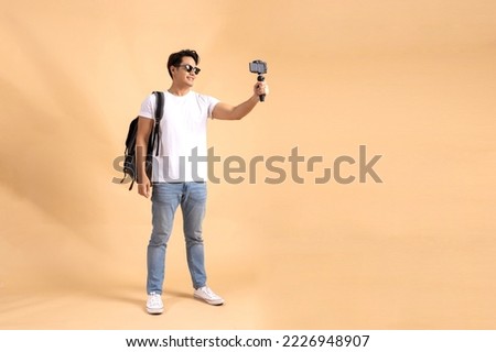 Young Asian tourist backpacker man smiling and taking a selfie and blog isolated on beige background Royalty-Free Stock Photo #2226948907