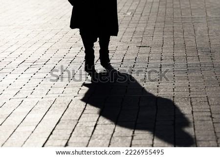 Black silhouette and shadow of lonely woman walking on a street. Female legs on paved city sidewalk