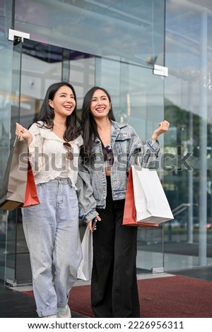 Portrait, Two joyful and attractive young Asian female friends walking out of the shopping mall with their shopping bags, had a fun shopping time together.